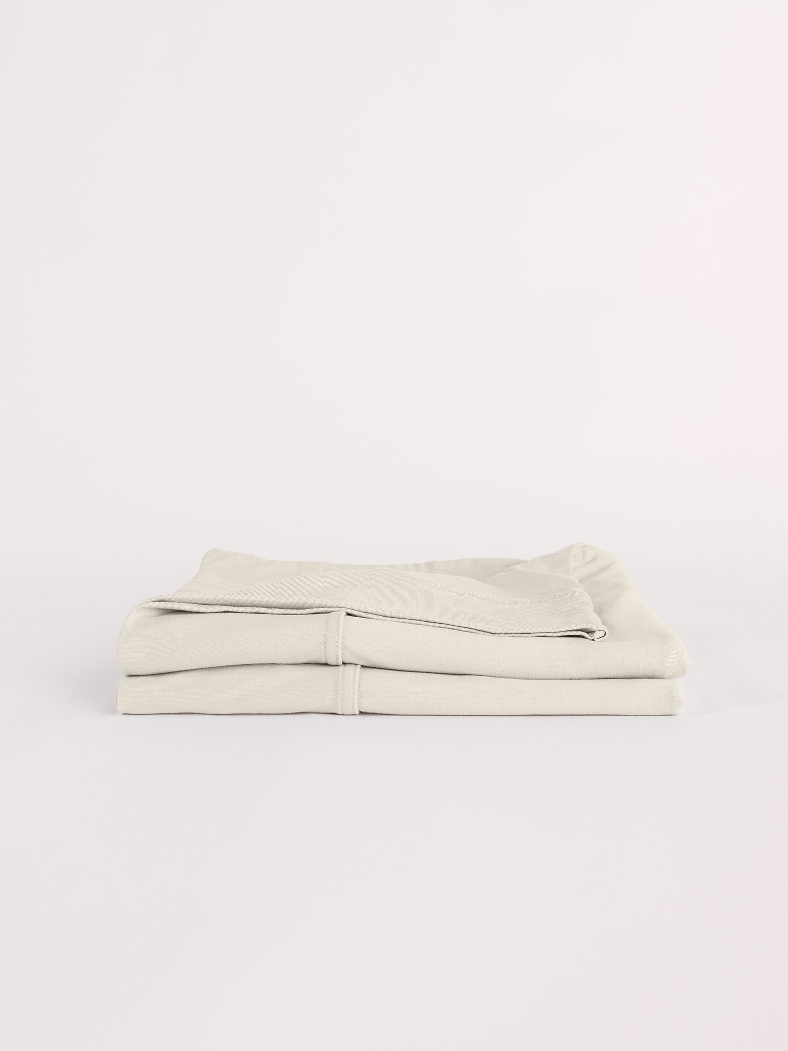 A neatly folded, light beige Bamboo Jersey Flat Sheet by Cozy Earth, displayed against a plain white background.|Color:Birch