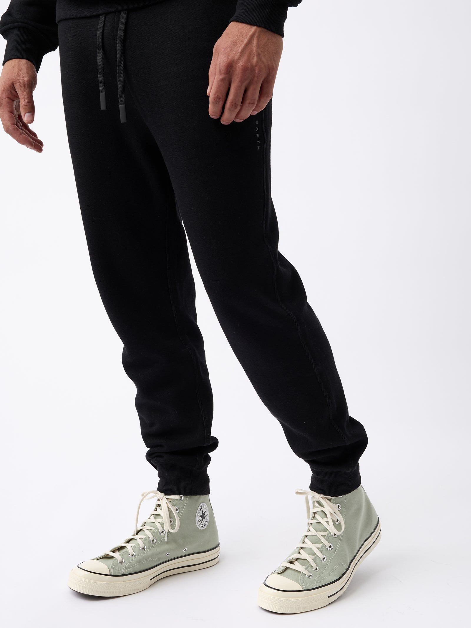 A person wearing Cozy Earth's Men's CityScape Jogger pants and light green high-top sneakers with white laces and soles stands on a white background, with only the lower body visible. 