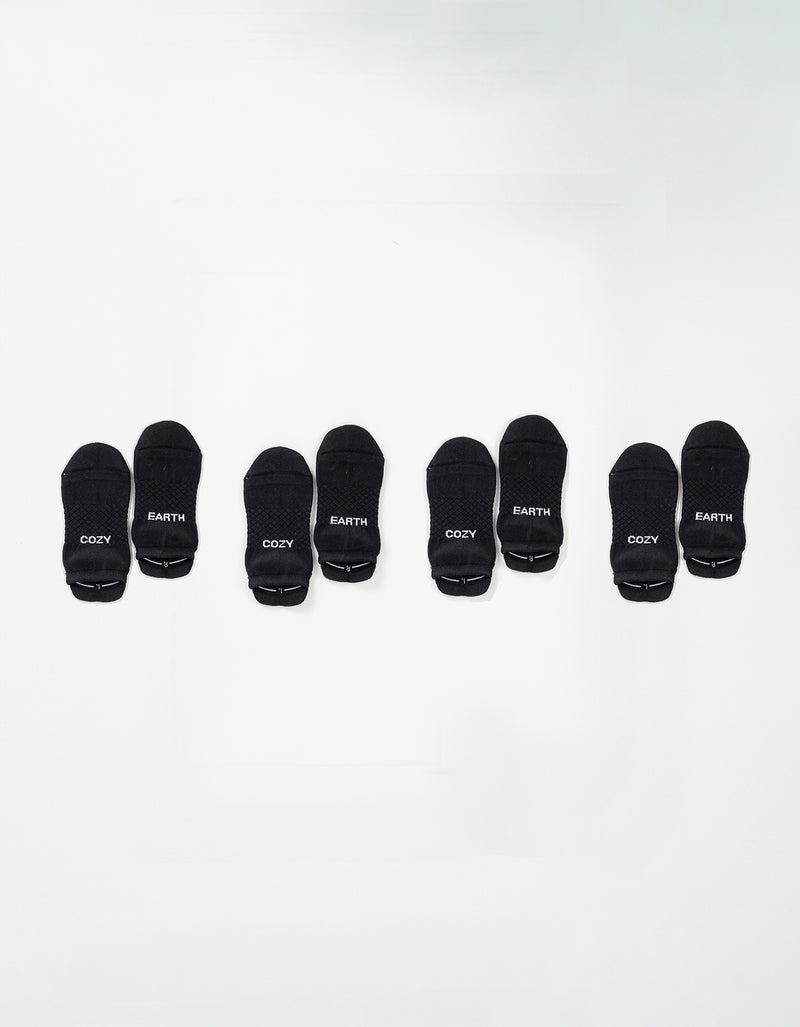 Four pairs of black Essential Ankle Socks by Cozy Earth are arranged in a row on a white background, each pair featuring "COZY" and "EARTH" in white text on the toes.