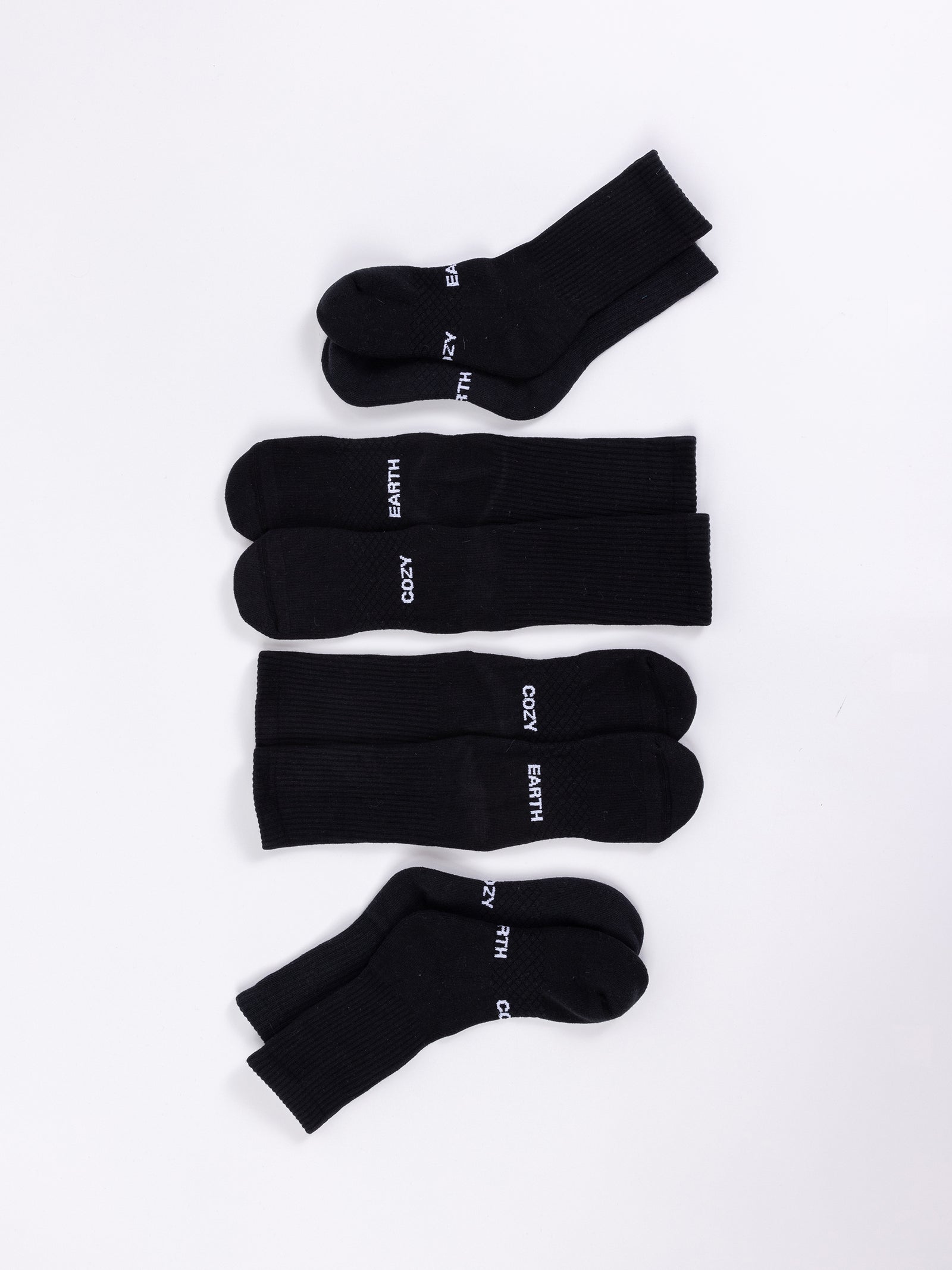 Four pairs of Essential Calf Socks by Cozy Earth, all in black, are laid out on a white background. The socks are positioned parallel to each other, with each pair slightly spaced apart. 