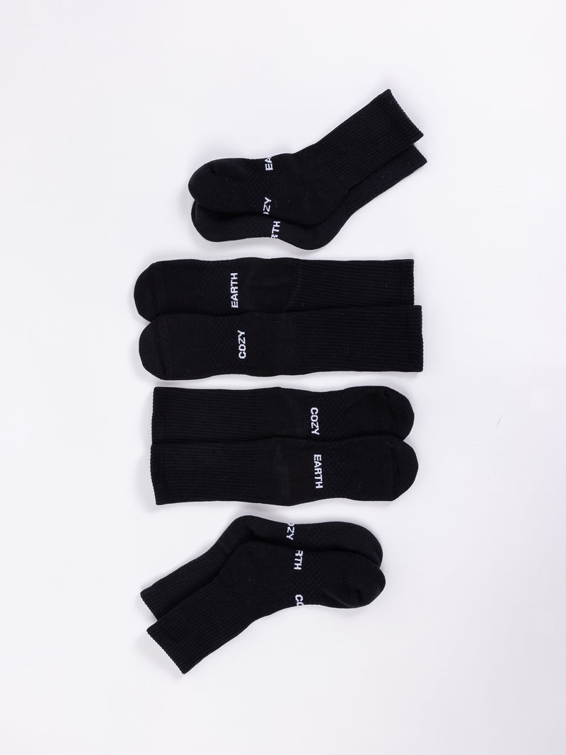 Four pairs of Essential Calf Socks by Cozy Earth, all in black, are laid out on a white background. The socks are positioned parallel to each other, with each pair slightly spaced apart.