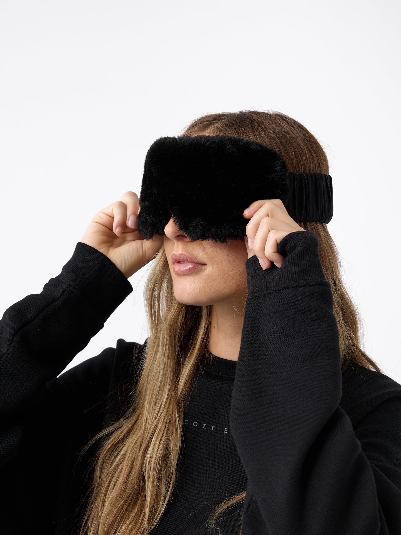 A woman wears the Cozy Earth Faux Fur Sleep Mask in Black. 