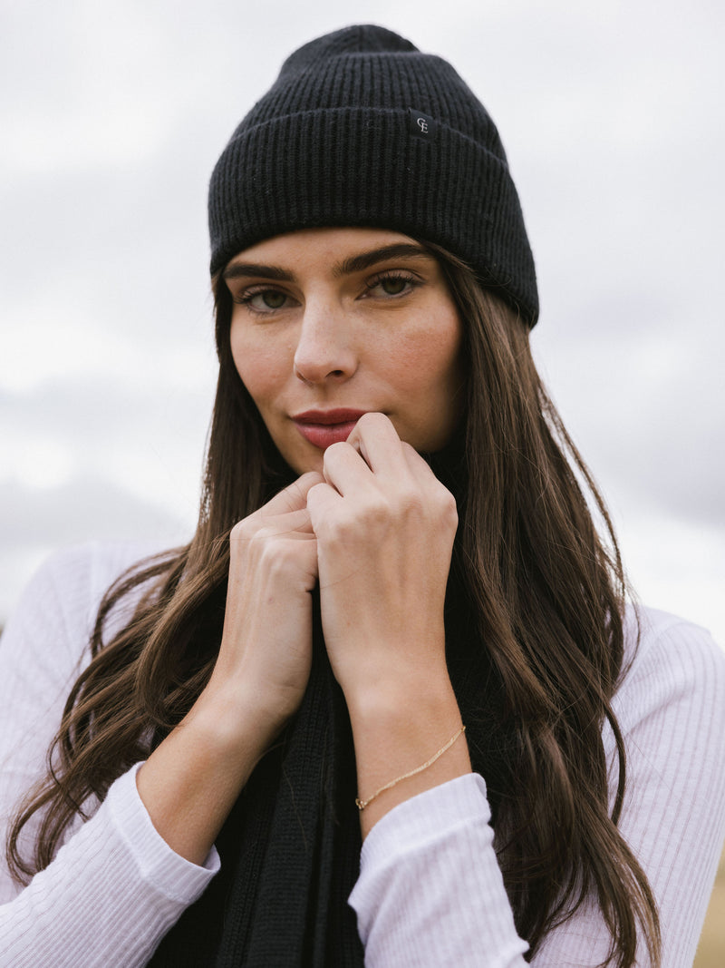 Woman wearing a black knit beanie and scarf on a white background