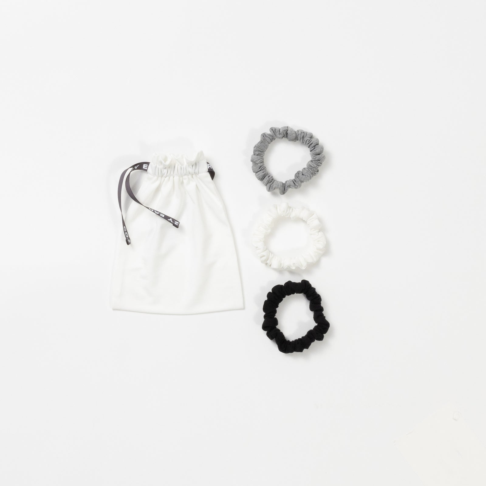 Cozy Earth Bamboo Stretch Knit Skinny Scrunchies in Grey, Ivory, and Black pictured with storage bag on a white background. 