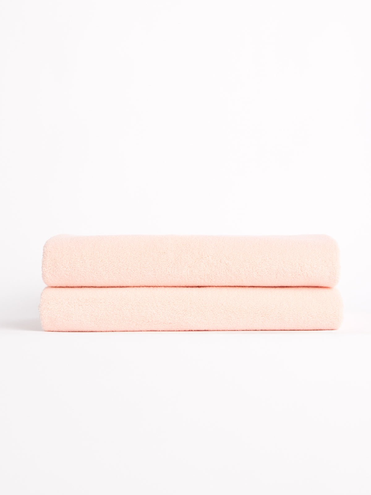 Two Luxe Bath Towels from Cozy Earth, neatly folded in light pink, stacked against a white background. 