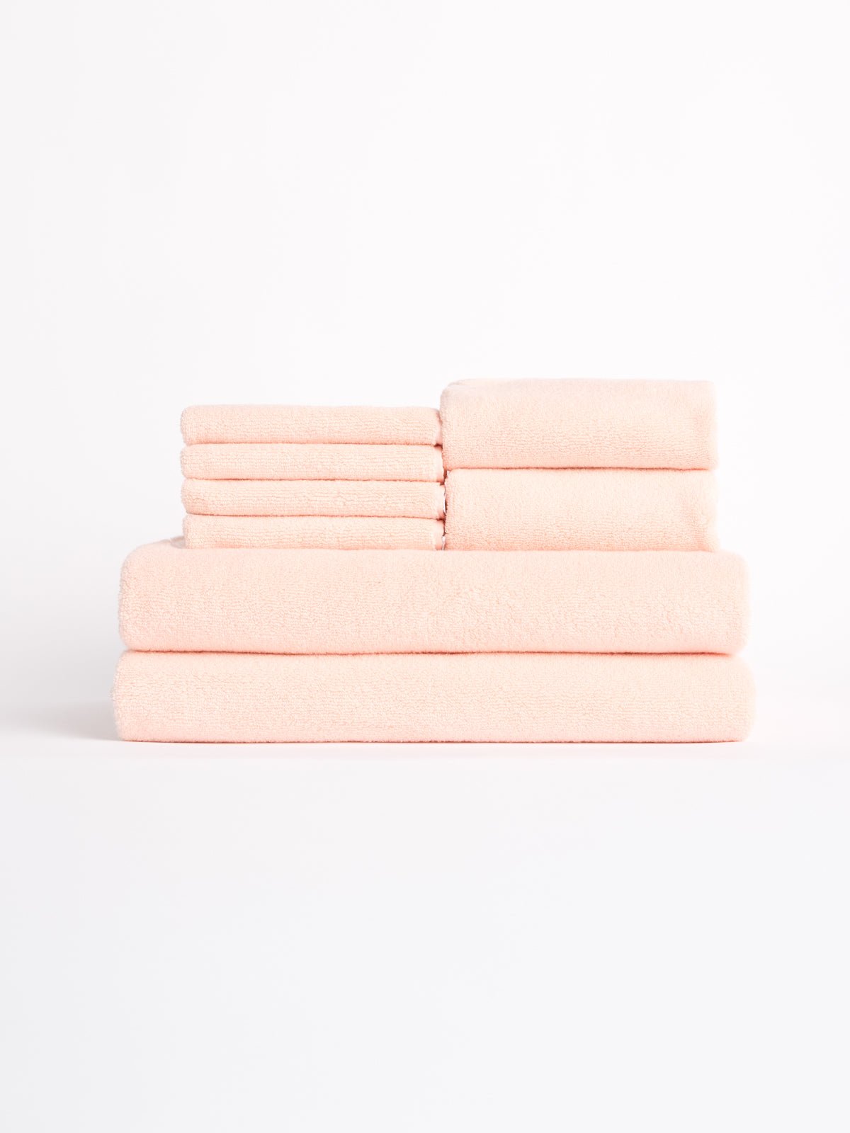 A neatly stacked Luxe Bath Towel Set by Cozy Earth, featuring soft, pale pink towels in various sizes, is arranged against a plain white background. 