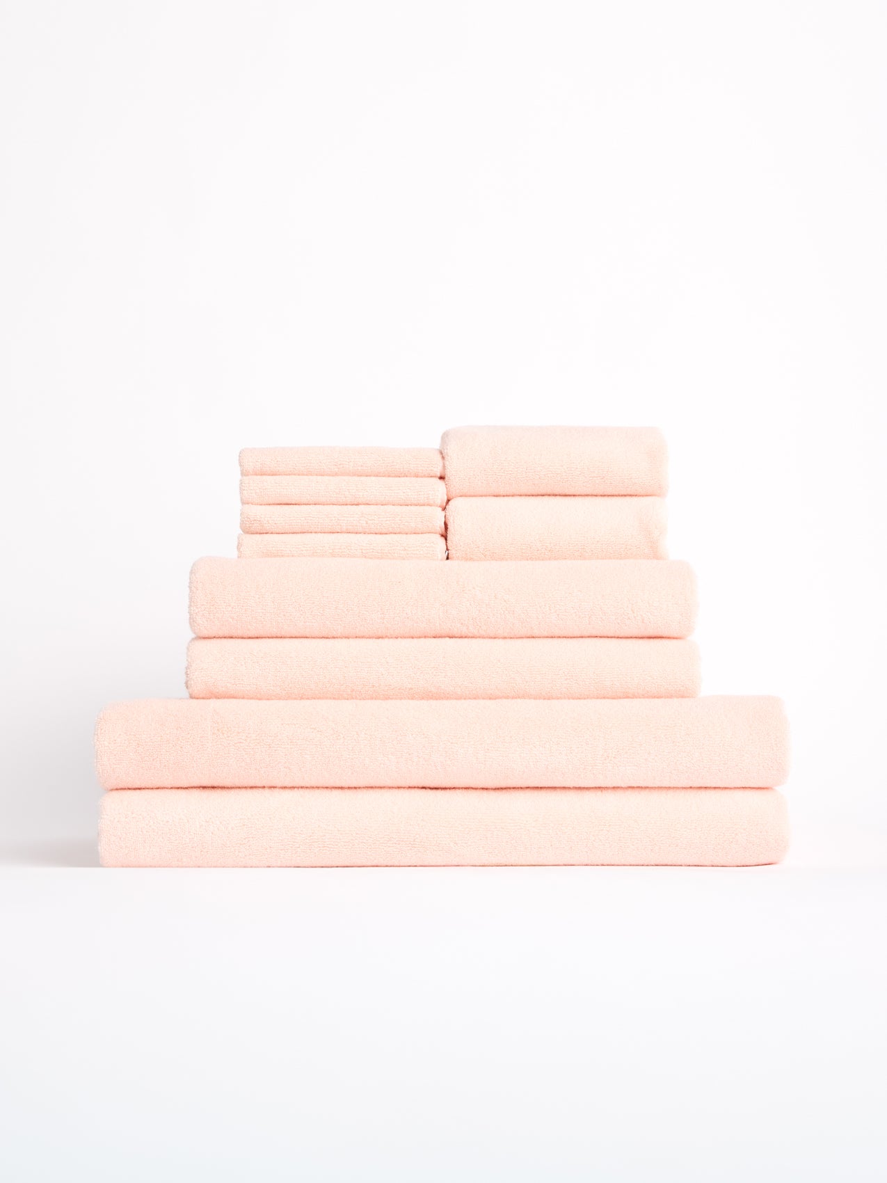 The Complete Luxe Bath Bundle by Cozy Earth features a neatly arranged stack of soft, peach-colored towels in decreasing size on a plain white background. 