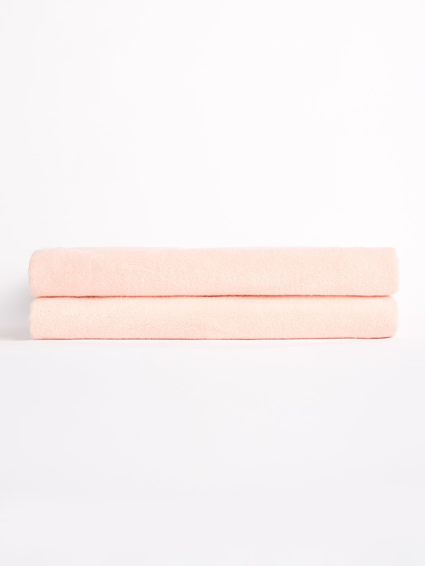 Two Luxe Bath Sheets by Cozy Earth, neatly folded and soft in pink, are stacked against a plain white backdrop. |Color:Blossom