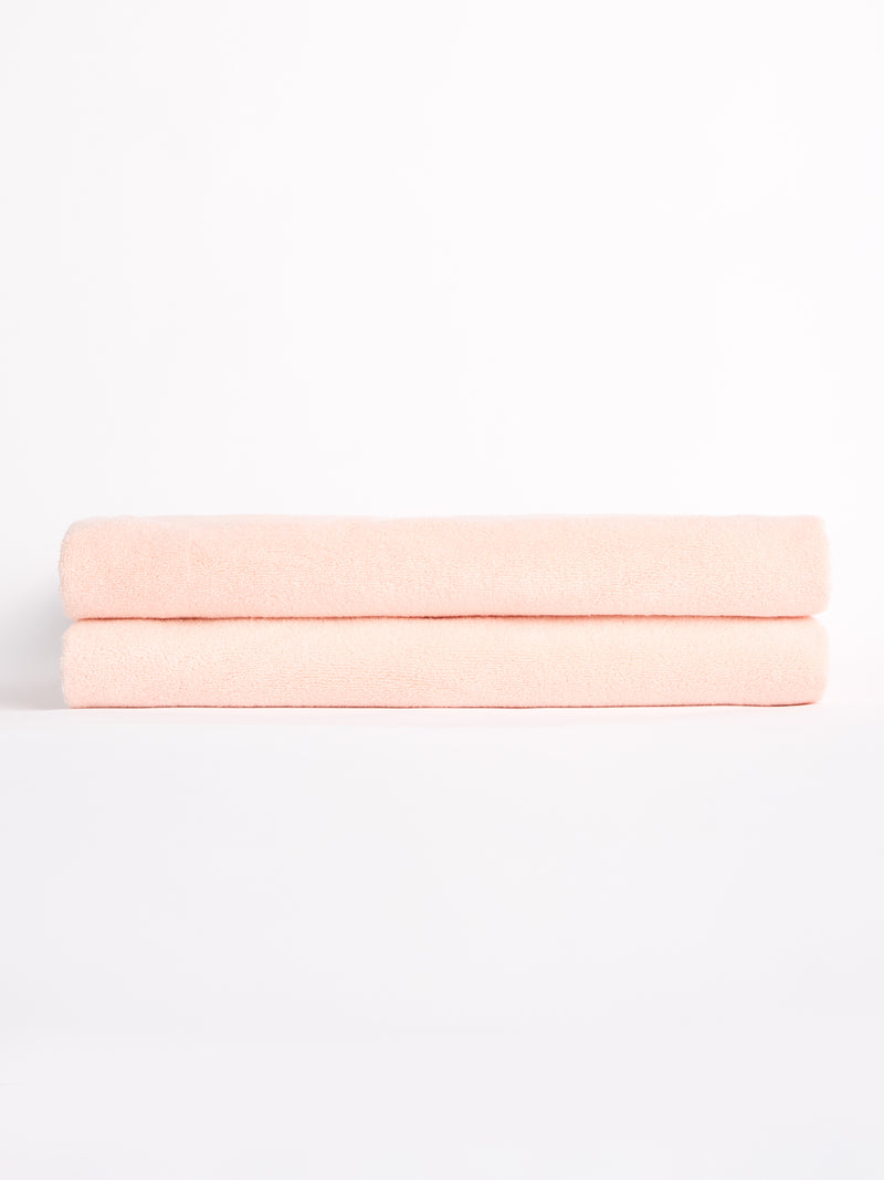Two Luxe Bath Sheets by Cozy Earth, neatly folded and soft in pink, are stacked against a plain white backdrop.