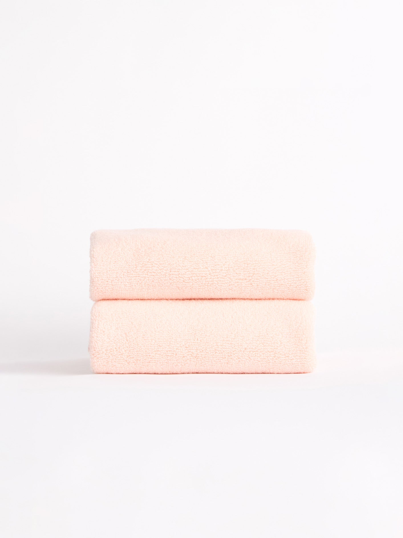 Two Luxe Hand Towels by Cozy Earth, in a soft pink hue, neatly folded and stacked against a white background. |Color:Blossom