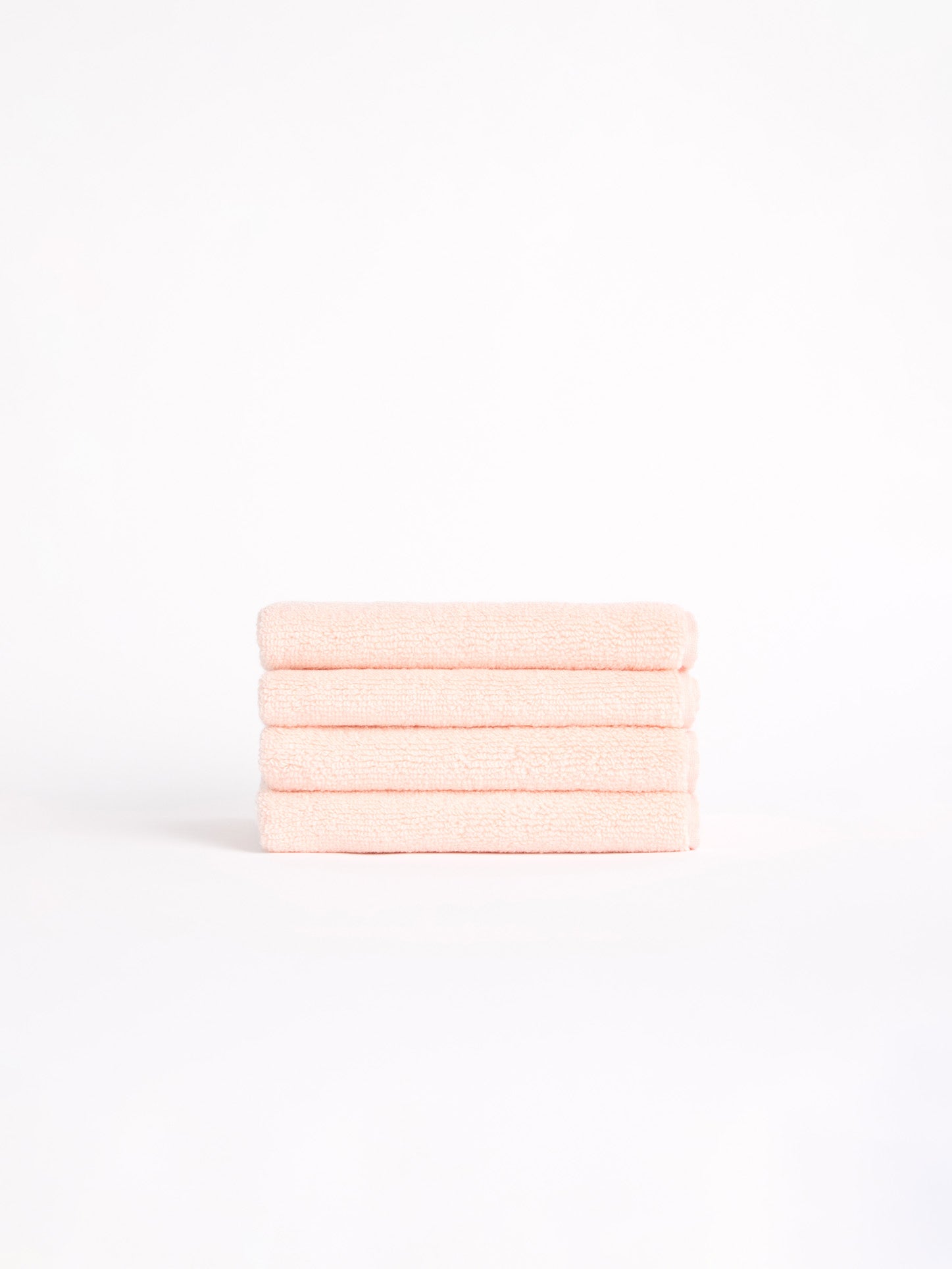 Four neatly folded Luxe Washcloths in light pink from Cozy Earth sit against a plain white backdrop. 