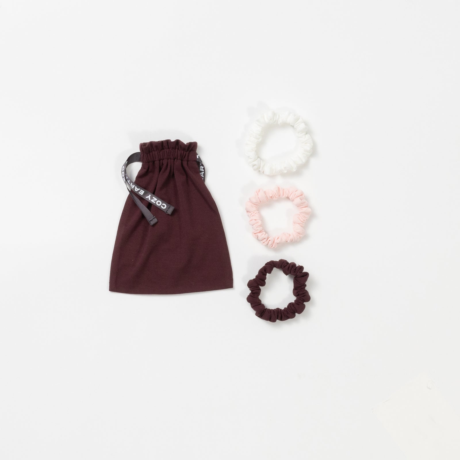 Cozy Earth Bamboo Stretch Knit Skinny Scrunchies in Ivory, Blossom, and Burgundy pictured with storage bag on a white background. 