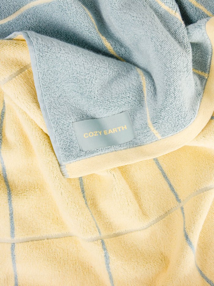 The Windowpane Resort Towel by Cozy Earth features a soft, light yellow and gray checkered design with a "COZY EARTH" tag on the corner. 