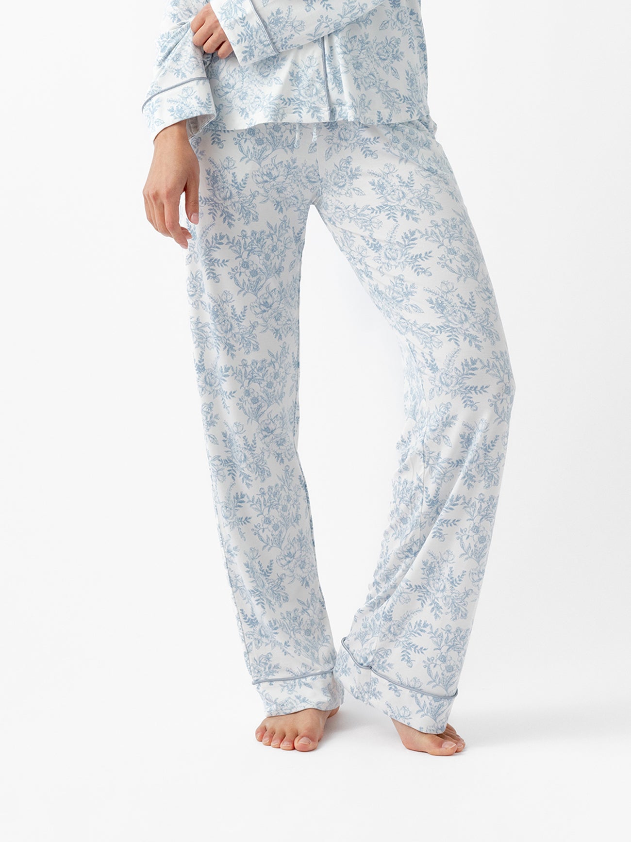 A person stands barefoot wearing Cozy Earth Women's Bamboo Stretch-Knit Pajama Pant in a blue floral pattern with long sleeves, shown against a plain white background. The image focuses on the lower half of the body. 