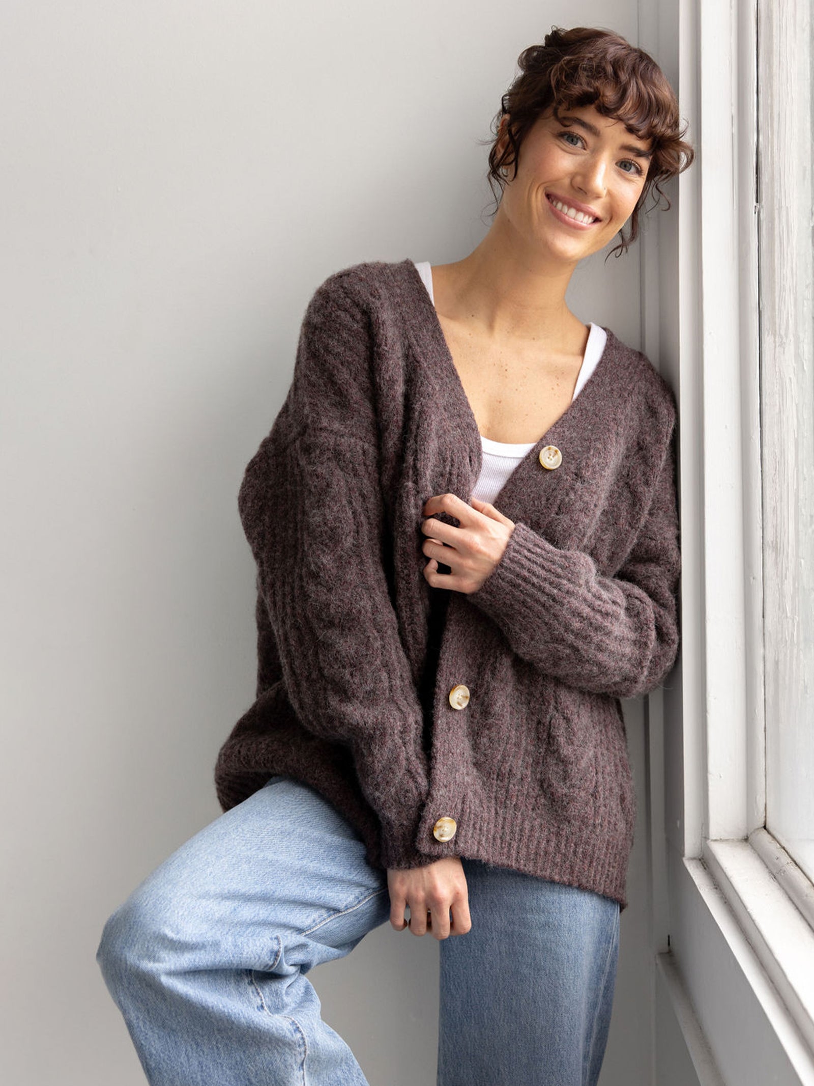 Woman wearing bordeaux cardigan and jeans in front of wall 