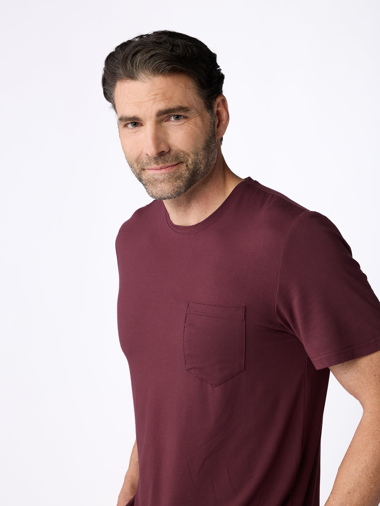 A man with short, dark hair and a beard is wearing the Cozy Earth Men's Stretch-Knit Bamboo Lounge Tee in maroon, standing against a plain white background. 