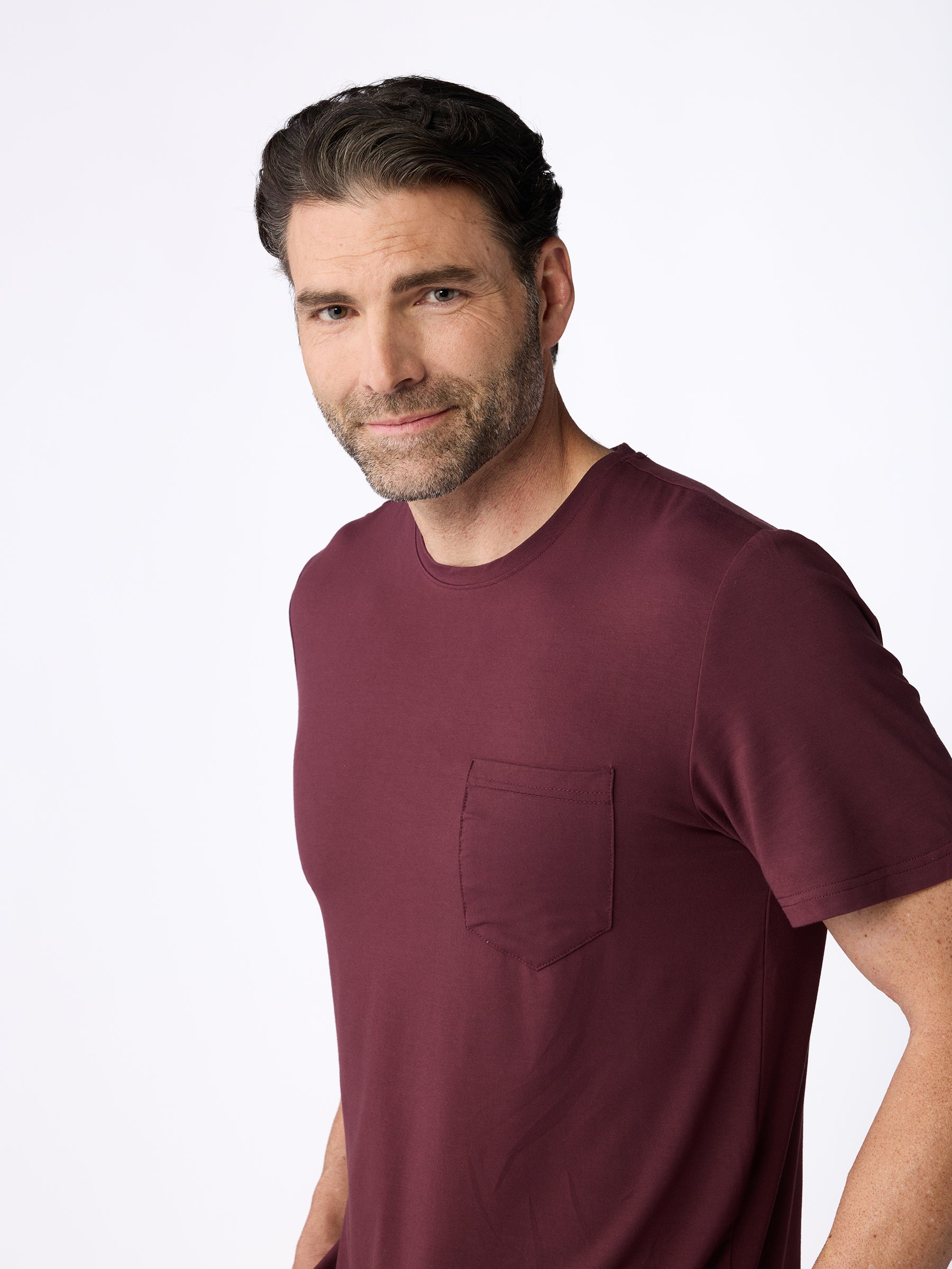 A man with short, dark hair and a beard is wearing the Cozy Earth Men's Stretch-Knit Bamboo Lounge Tee in maroon, standing against a plain white background. |Color:Burgundy