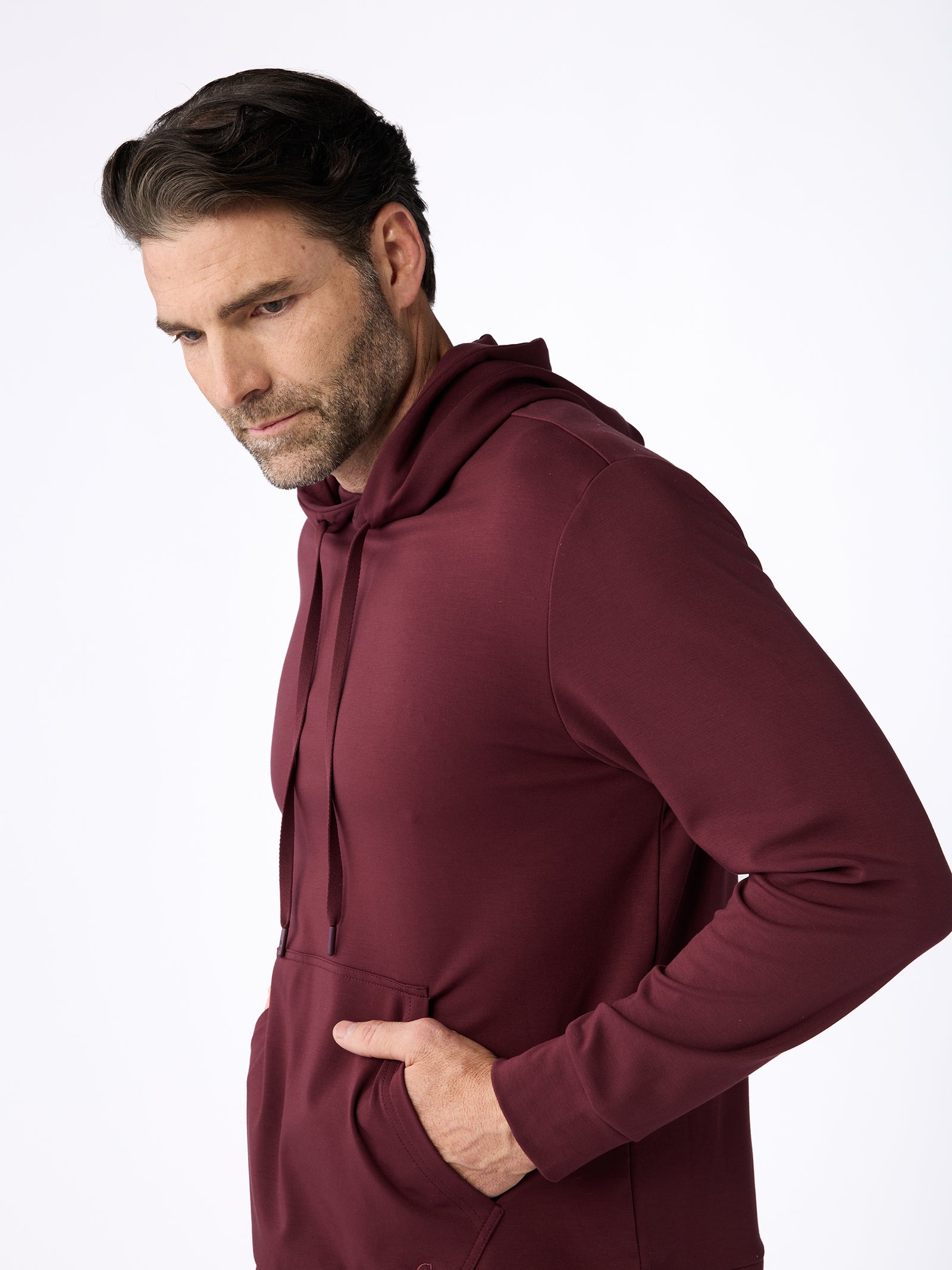 A man wearing the Men's Ultra-Soft Bamboo Hoodie by Cozy Earth, with his hands in the front pocket and looking thoughtful, is set against a plain white background. 