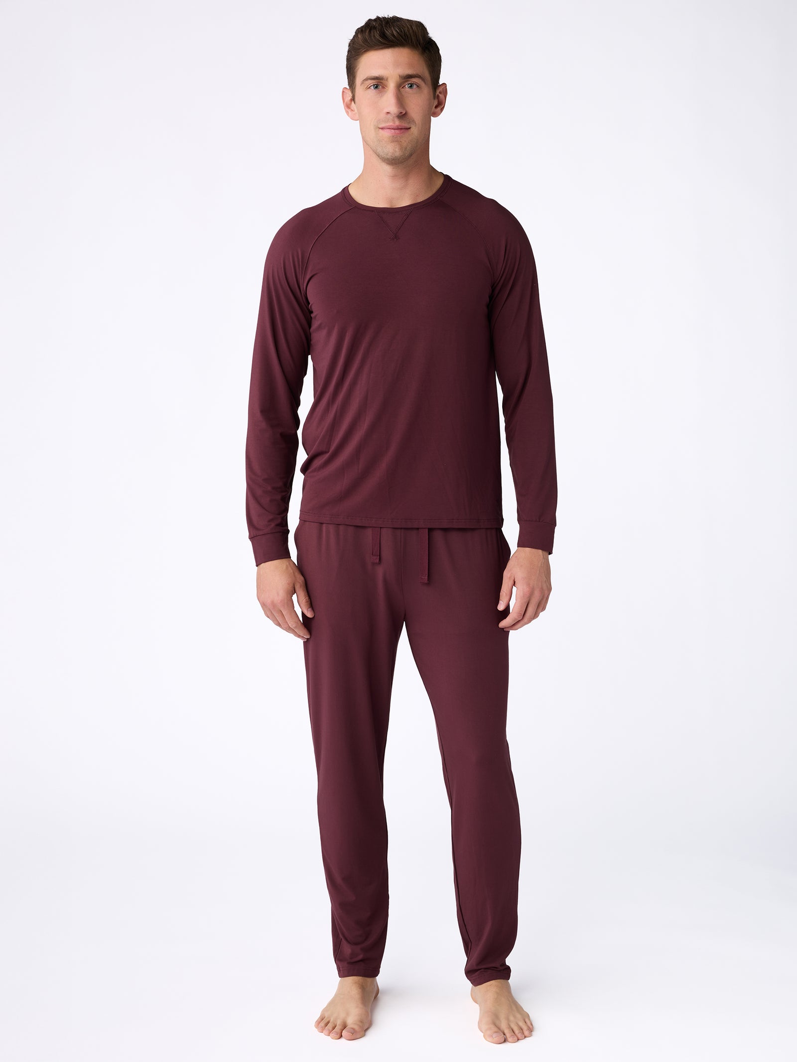 A man stands barefoot on a plain white background wearing a matching maroon Men's Ultra-Soft Bamboo Pullover Crew by Cozy Earth. He is facing forward with a neutral expression. 