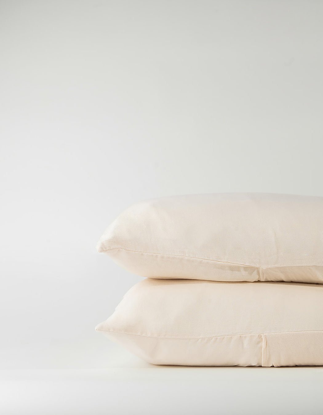 Two Aire Bamboo Shams by Cozy Earth are stacked against a plain, light background. Their cream color, smooth and soft texture, and simple edge stitching are on display.