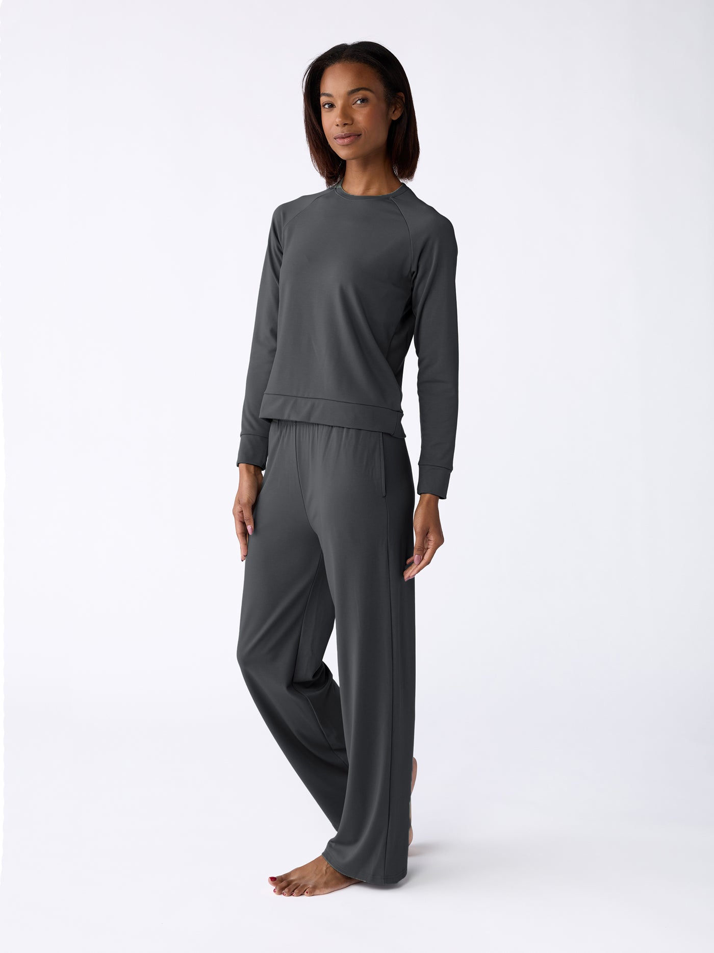 Standing barefoot against a plain white background, a person wears the Cozy Earth Women's Ultra-Soft Bamboo Wide Leg Pull On Pant & Pullover Crew Set in dark gray and looks forward with a relaxed posture. |Color:Charcoal