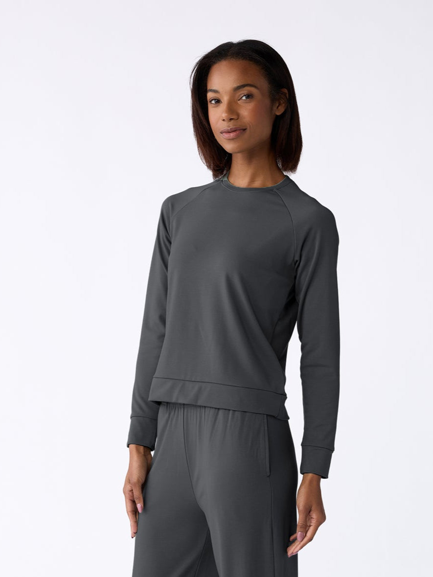 Standing barefoot against a plain white background, a person wears the Cozy Earth Women's Ultra-Soft Bamboo Wide Leg Pull On Pant & Pullover Crew Set in dark gray and looks forward with a relaxed posture. 