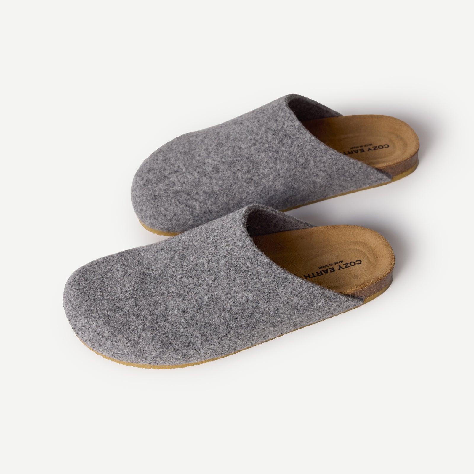 The Lakehouse Clog by Cozy Earth features a minimalist design with grey woolen uppers and natural brown soles. It has a closed toe, open back, and is ideal for indoor wear. A logo is visible on the insole, all showcased on a white background. 