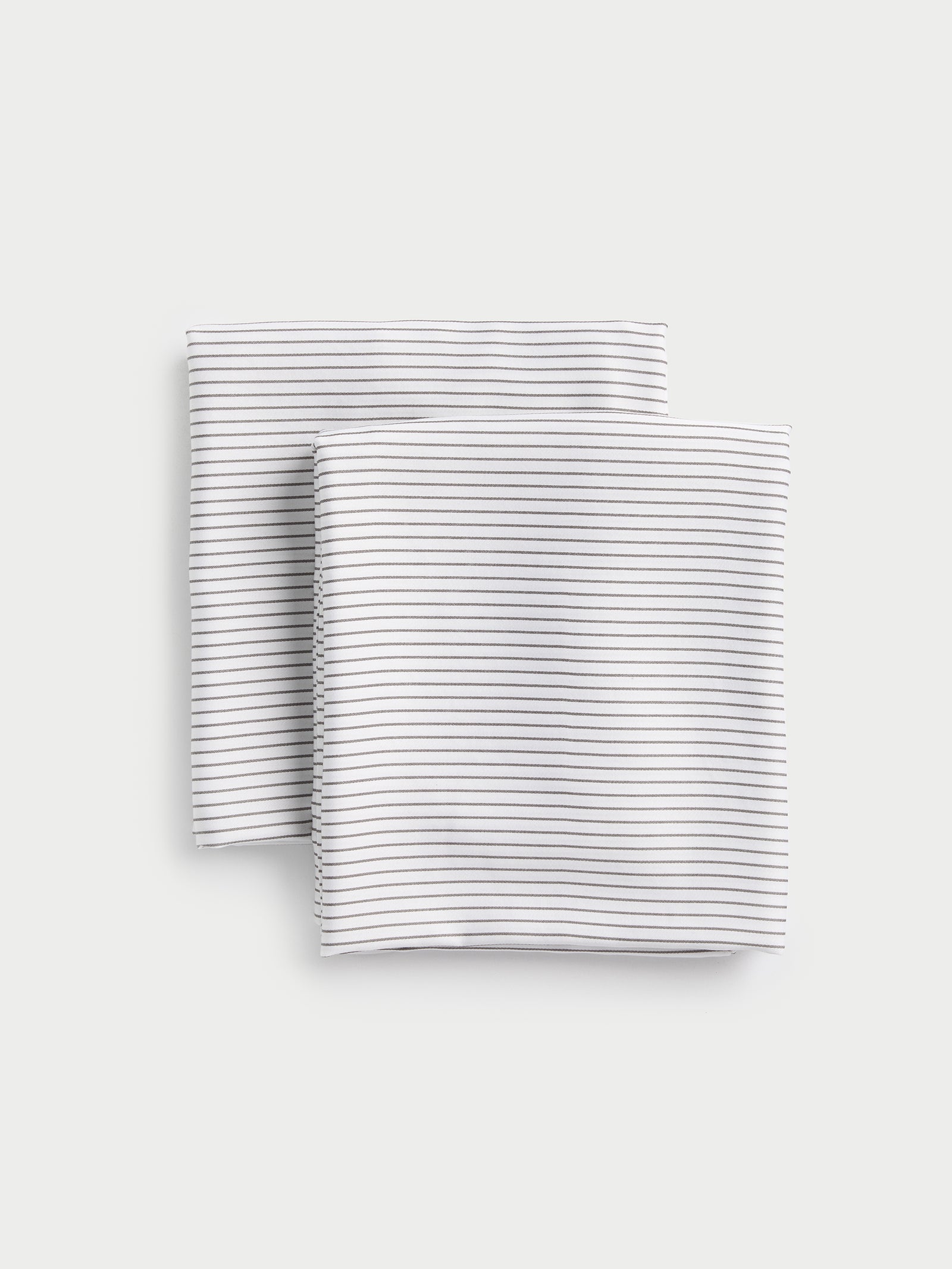 Two neatly folded Bamboo Pillowcases from Cozy Earth, featuring thin black horizontal stripes, are placed side by side on a plain white background. 