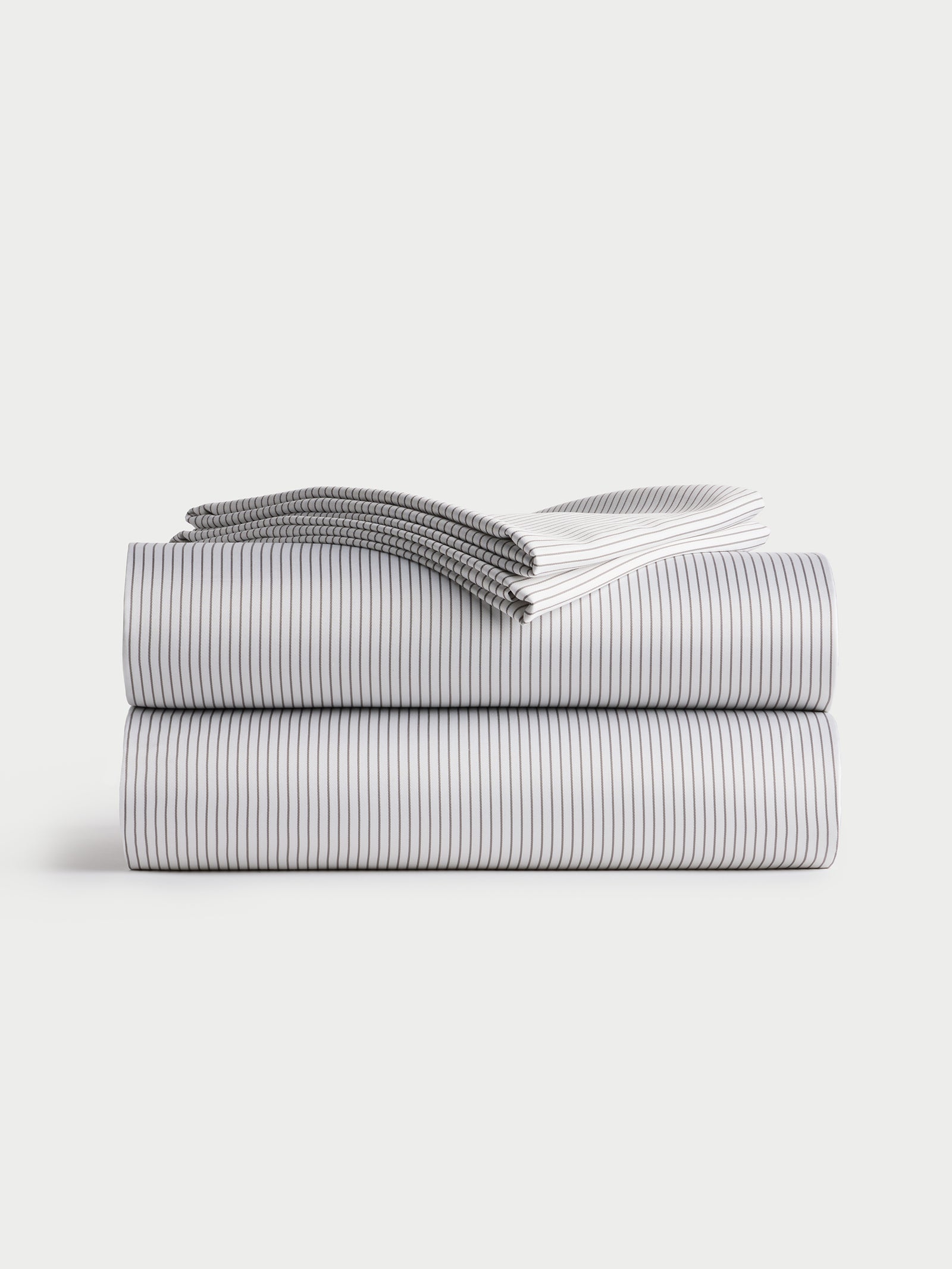 A neatly folded stack of Bamboo Sheet Sets from Cozy Earth, featuring a subtle black and white striped pattern. The sheets are arranged in a minimalist style on a plain white background. 