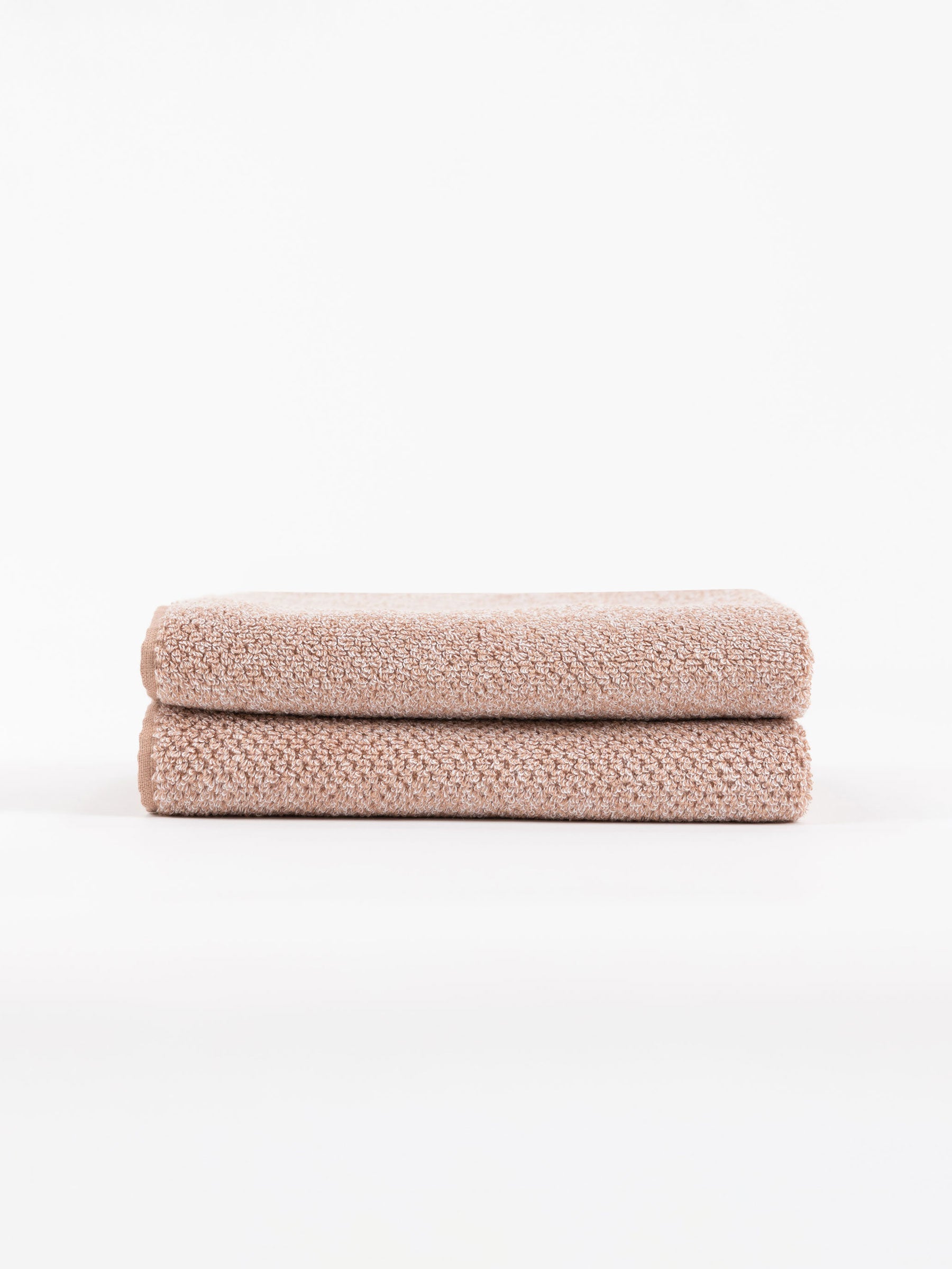 A pair of Nantucket Hand Towels in Heathered Clay is stacked in front of a white background. 