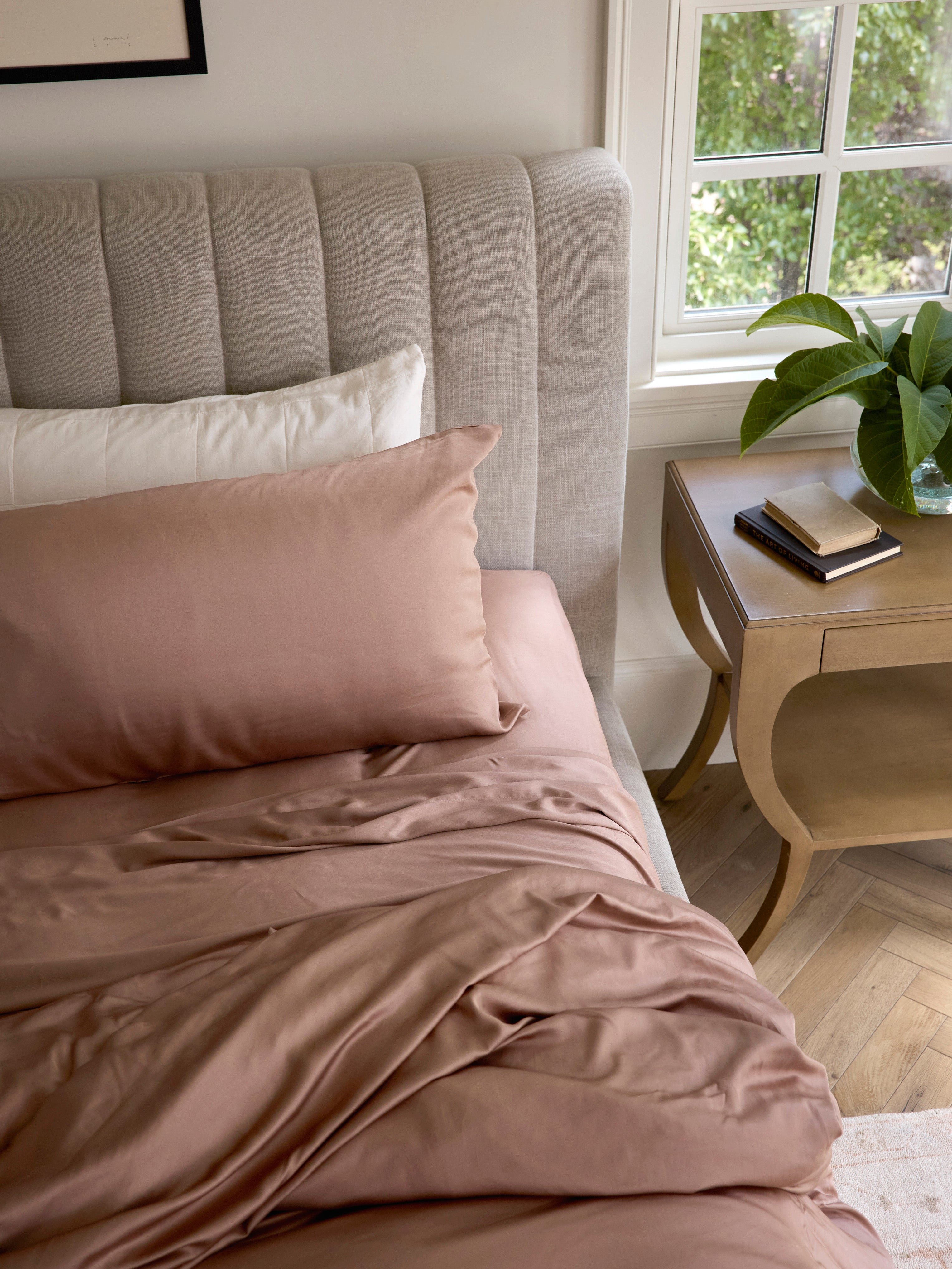 Clay bedding on unmade bed with books on the nightstand 