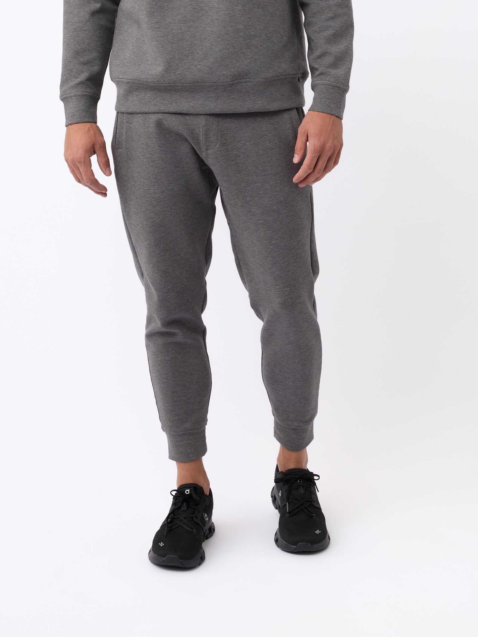 A person wearing Cozy Earth's Men's StretchTech Jogger and black sneakers is standing against a plain white background, with the image focusing on the lower half of the body. 