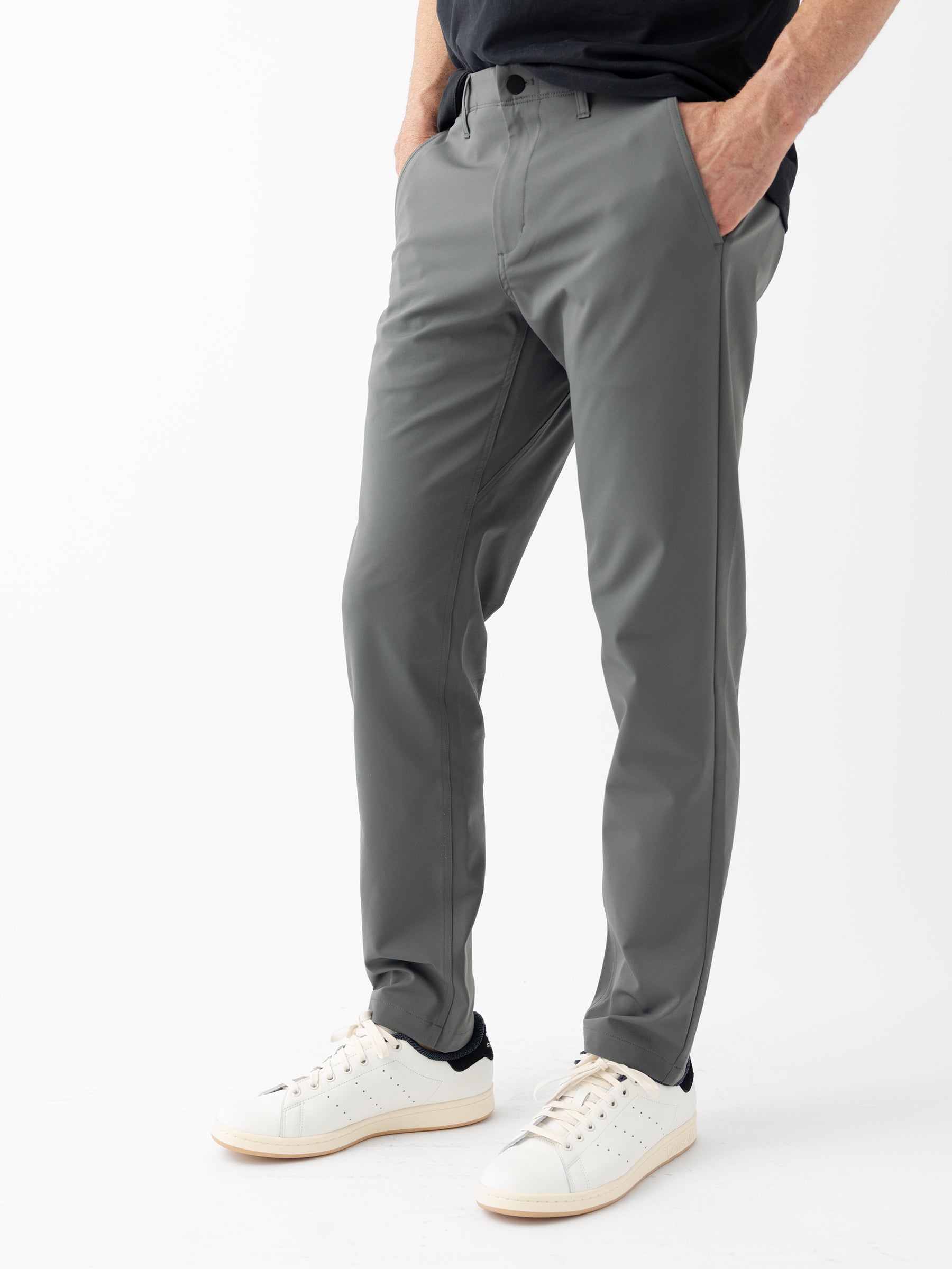 A person stands with hands in pockets, wearing Men's Everywhere Pant 30L from Cozy Earth and white sneakers with black accents. The photo is cropped at the torso and focuses on the pants and shoes, set against a plain white background. |Color:Coal