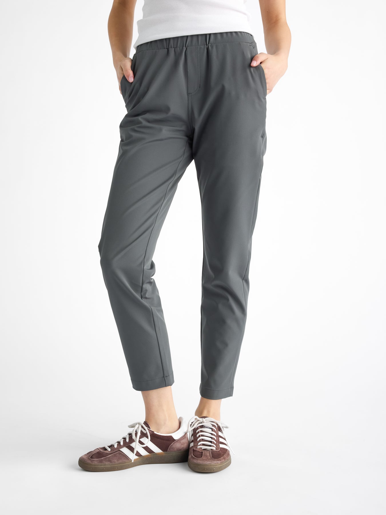 A woman stands with hands in pockets against a plain white background wearing Cozy Earth's Women's Always Cropped Pant and brown sneakers with white laces. |Color:Coal