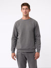 A man is wearing the Men's StretchTech Crewneck sweatshirt from Cozy Earth, paired with matching sweatpants. He stands against a plain white background with short brown hair, looking forward with a neutral expression. |Color:Coal Heather