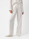 A person wearing Cozy Earth's Women's Soft Woven Pajama Pant, featuring a white fabric with vertical red and green stripes, paired with a matching long-sleeved top. They are standing against a plain white background and wearing light-colored socks. |Color:Cottage Stripe