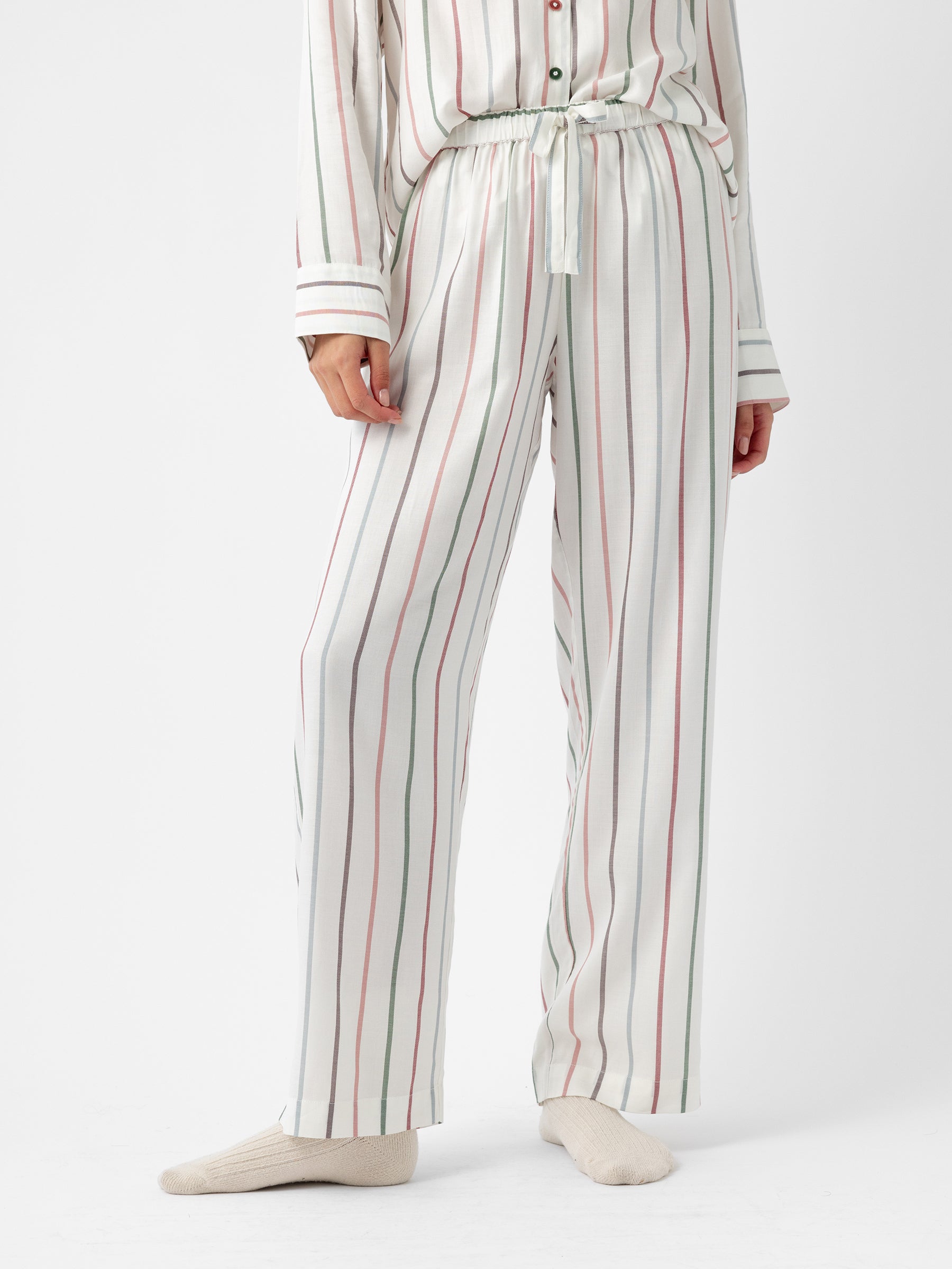 A person wearing Cozy Earth's Women's Soft Woven Pajama Pant, featuring a white fabric with vertical red and green stripes, paired with a matching long-sleeved top. They are standing against a plain white background and wearing light-colored socks. |Color:Cottage Stripe