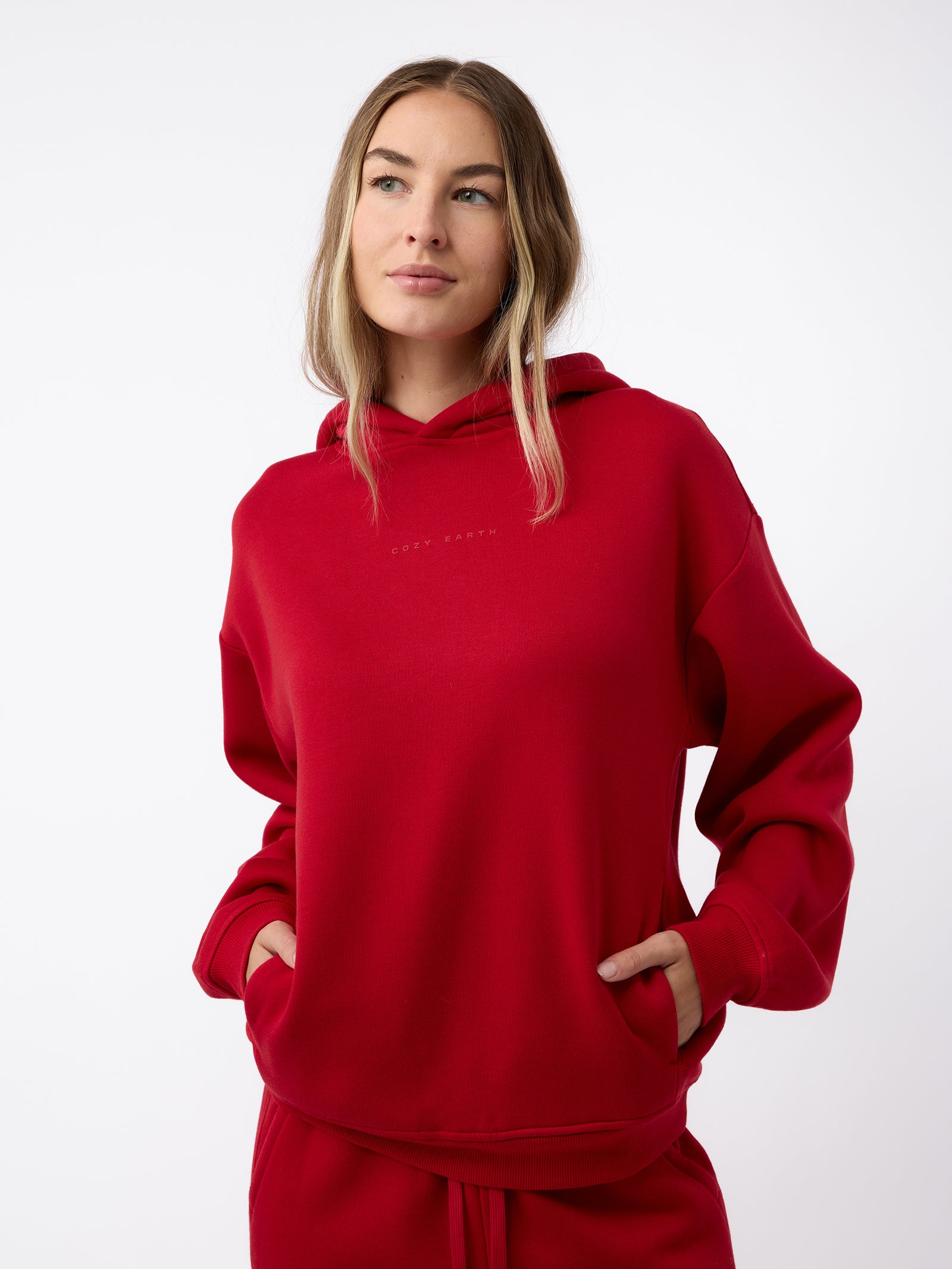 A person wearing the Women's CityScape Hoodie by Cozy Earth, with hands in the pockets, stands against a white background. They have long, light brown hair and are looking slightly to the side. 