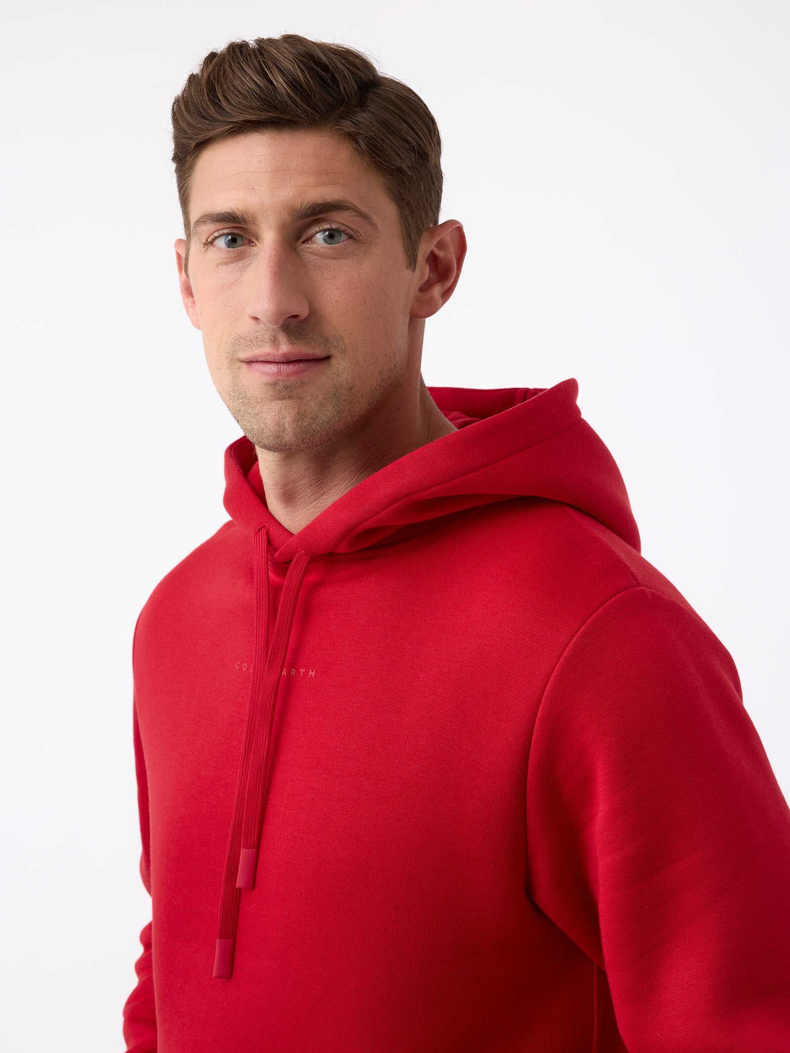 A person wearing a vibrant Men's CityScape Hoodie from Cozy Earth stands against a plain white background. They have short brown hair and are looking directly at the camera with a neutral expression. 