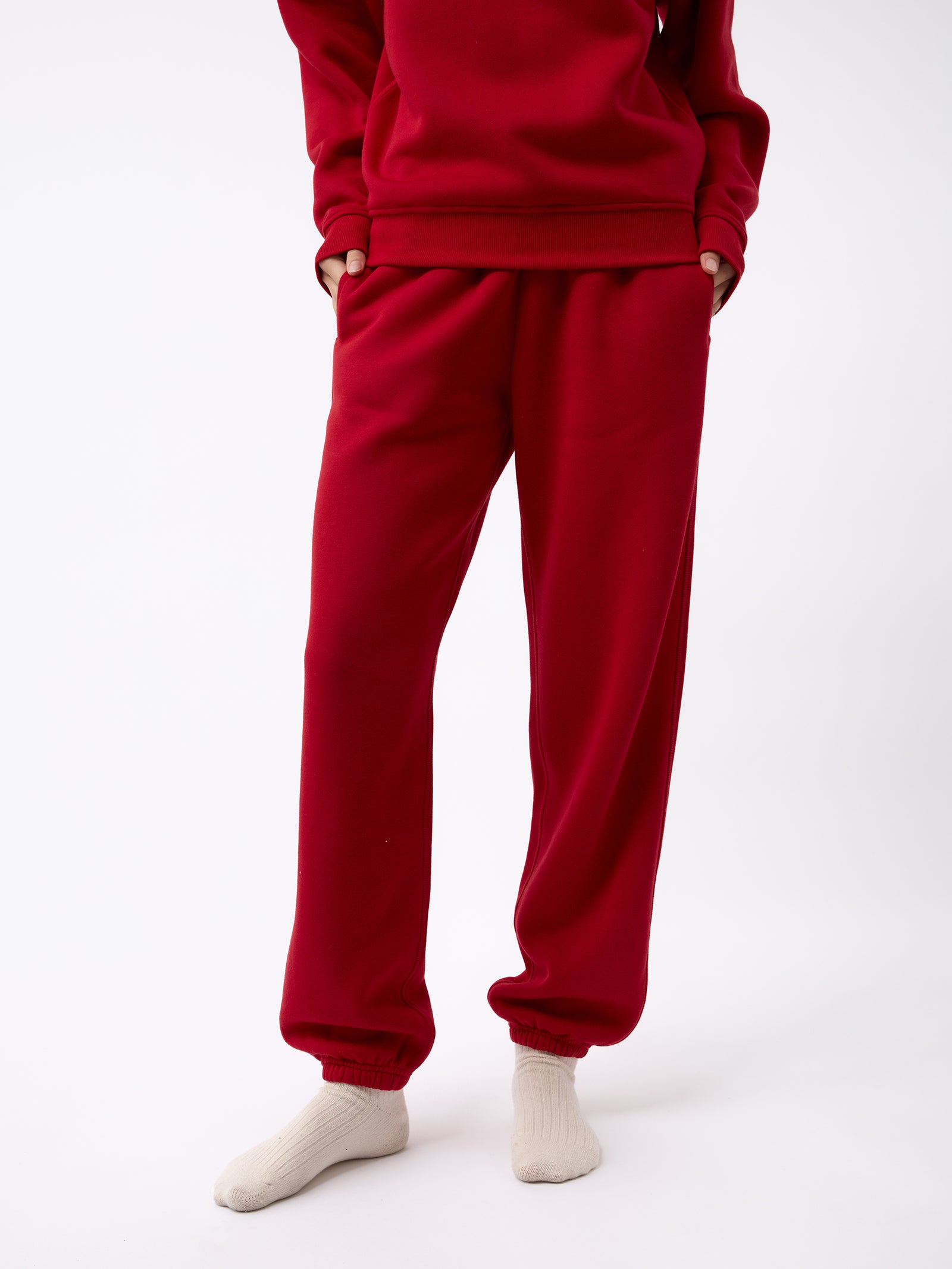 A person is wearing Cozy Earth's Women's CityScape Sweatpant in red, with their hands in the pockets, standing against a white background and feet adorned in white socks. 