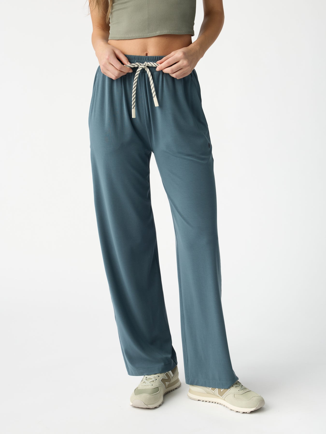 A woman models Cozy Earth's Women's Studio Wide Leg Pant in teal, paired with a green crop top and light beige sneakers. The photo is taken against a plain white background, focusing on the outfit while her face remains out of view. |Color:Dawn