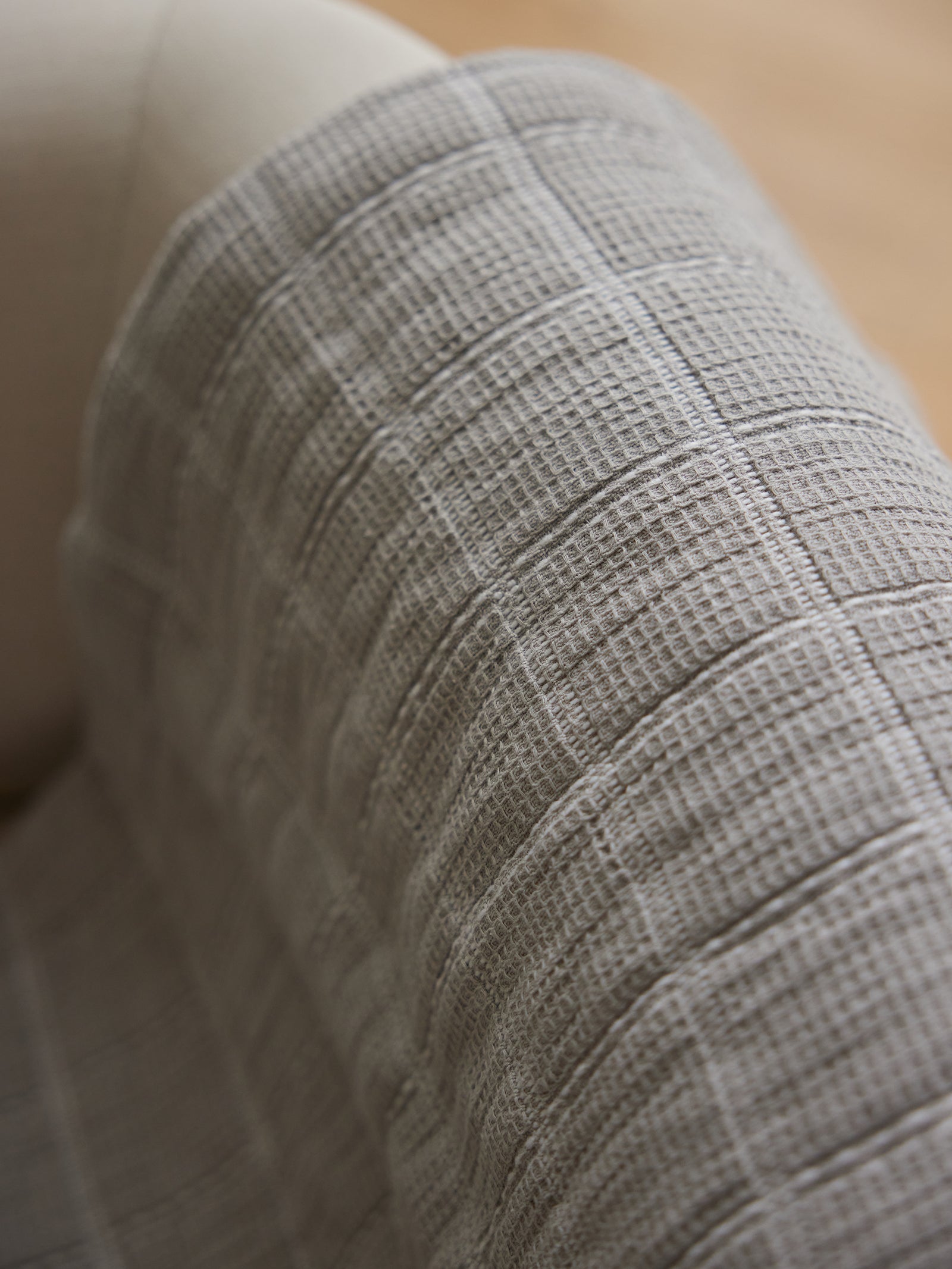 A close-up image of Cozy Earth's beige-colored Waffle Windowpane Blanket draped over part of a light-colored upholstered chair. The blanket's grid-like, waffle pattern creates a soft and cozy appearance. The background is softly blurred. 