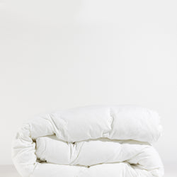 A neatly folded, fluffy white Down Alternative Comforter by Cozy Earth rests against a plain white background, showcasing its soft texture and inviting appearance.