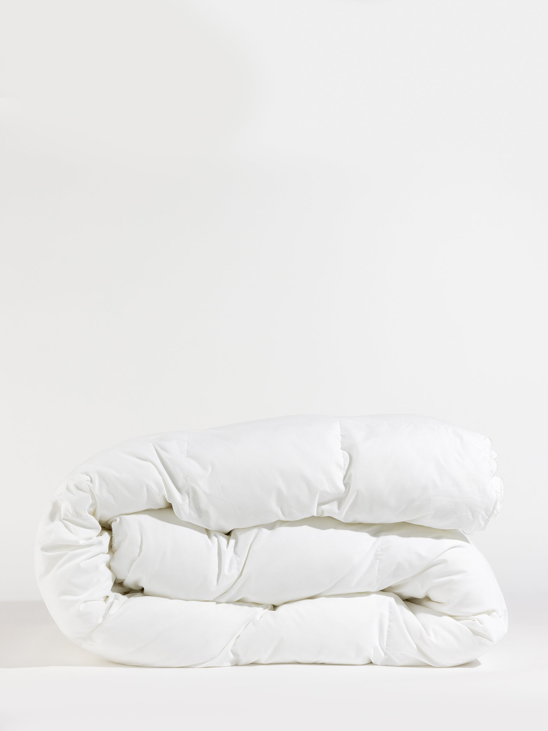 A neatly folded, fluffy white Down Alternative Comforter by Cozy Earth rests against a plain white background, showcasing its soft texture and inviting appearance.