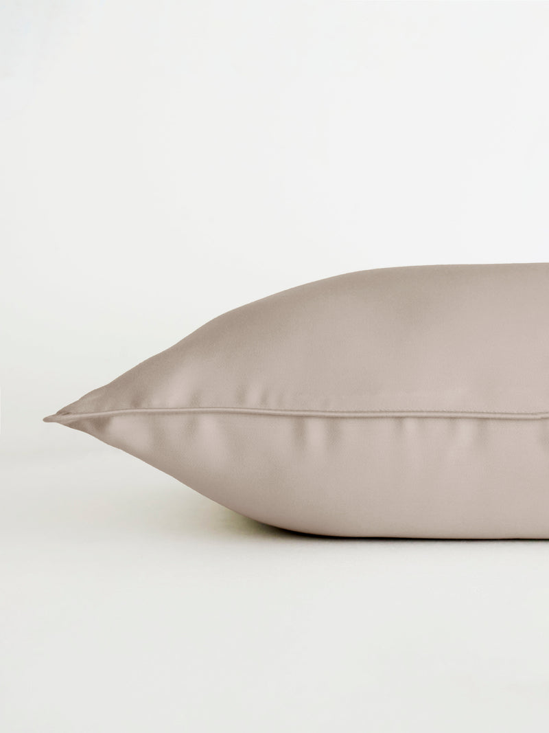 A close-up of a smooth, beige Bamboo Travel Pillowcase by Cozy Earth on a white surface. The pillowcase appears soft with a subtle sheen, highlighting its silky texture.