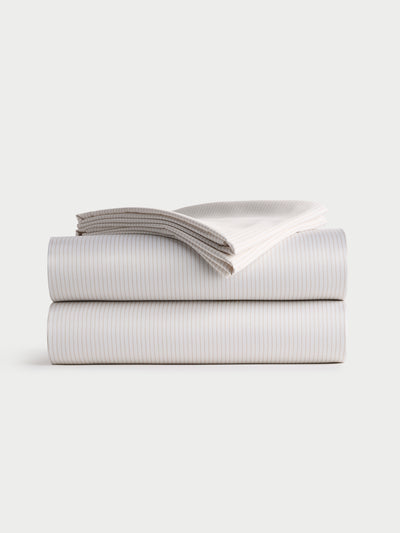 A neatly folded Bamboo Sheet Set by Cozy Earth, featuring a fitted sheet, flat sheet, and two pillowcases with a striped design, stacked on a plain white background. |Color:Driftwood Pinstripe