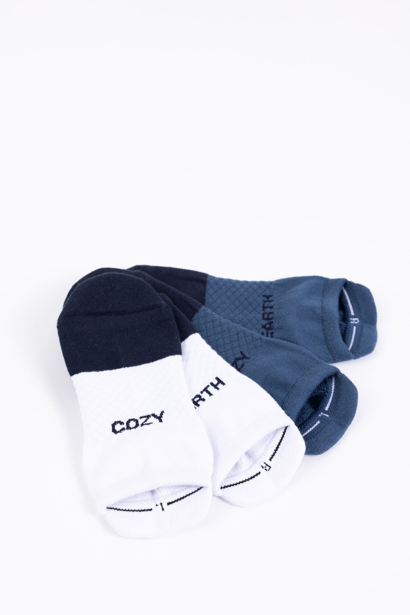 Pictured are a pair of color-blocked ankle socks from the Essential Ankle Sock 2-Pack by Cozy Earth. On the left, the black and white sock features the word "COZY," while on the right, the dark blue and light blue sock displays "EARTH." Both pairs are neatly placed next to each other. 