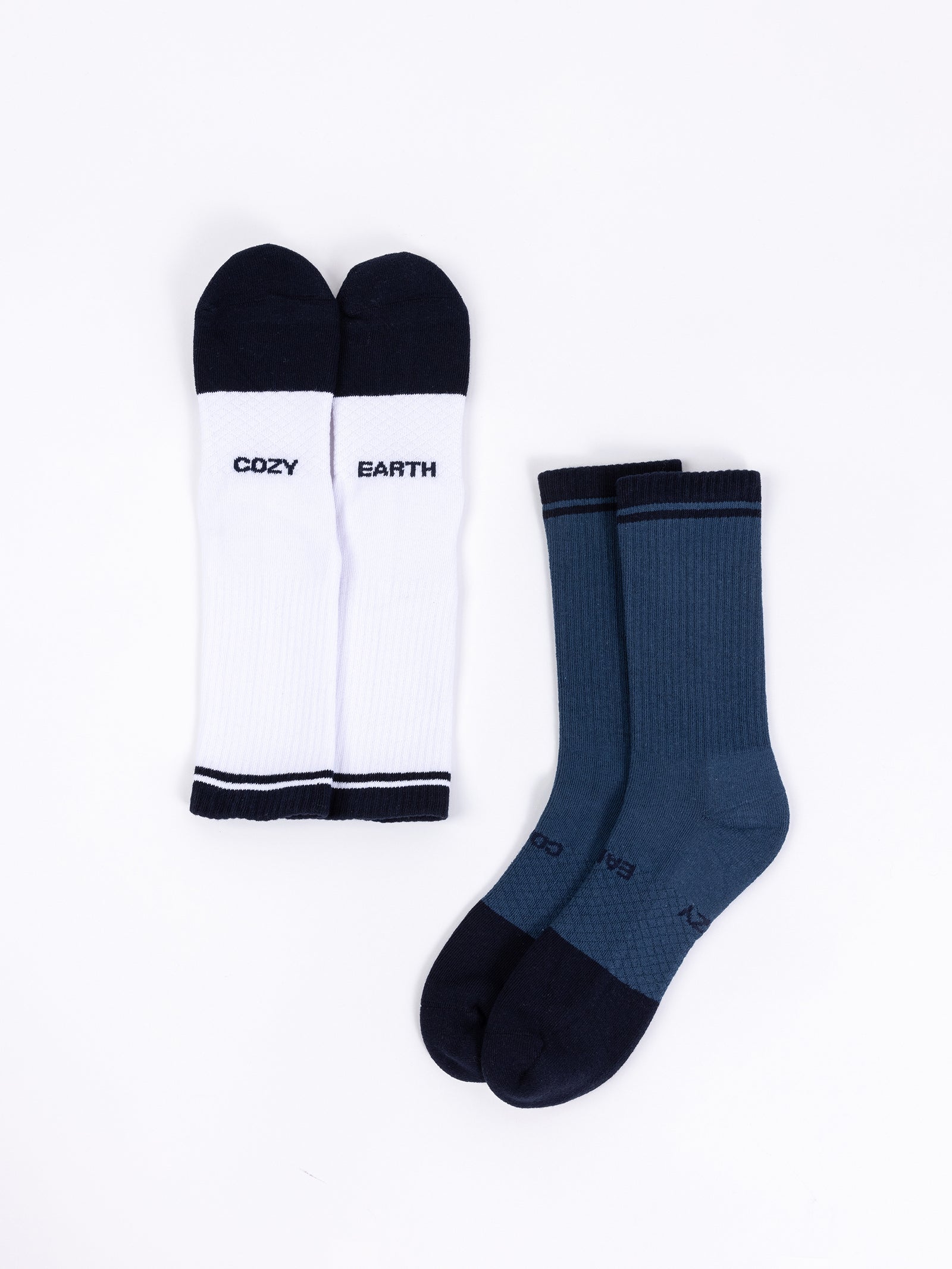 The Essential Calf Sock 2-Pack by Cozy Earth includes a white pair of crew socks with black tips, heels, and toes, featuring the words "COZY" and "EARTH" on each sock. This set also contains a blue pair of crew socks with dark tips, heels, and toes, all displayed against a white background. 