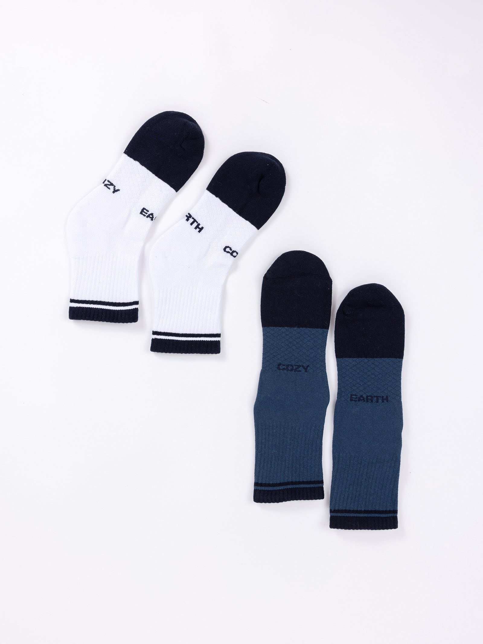 Two pairs of socks from the Essential Quarter Sock 2-Pack by Cozy Earth are displayed against a white background. The pair on the left is white and black with the words "COZY" and "EARTH" on the soles, while the pair on the right is blue and black with the same words, "COZY" and "EARTH," on their soles. 