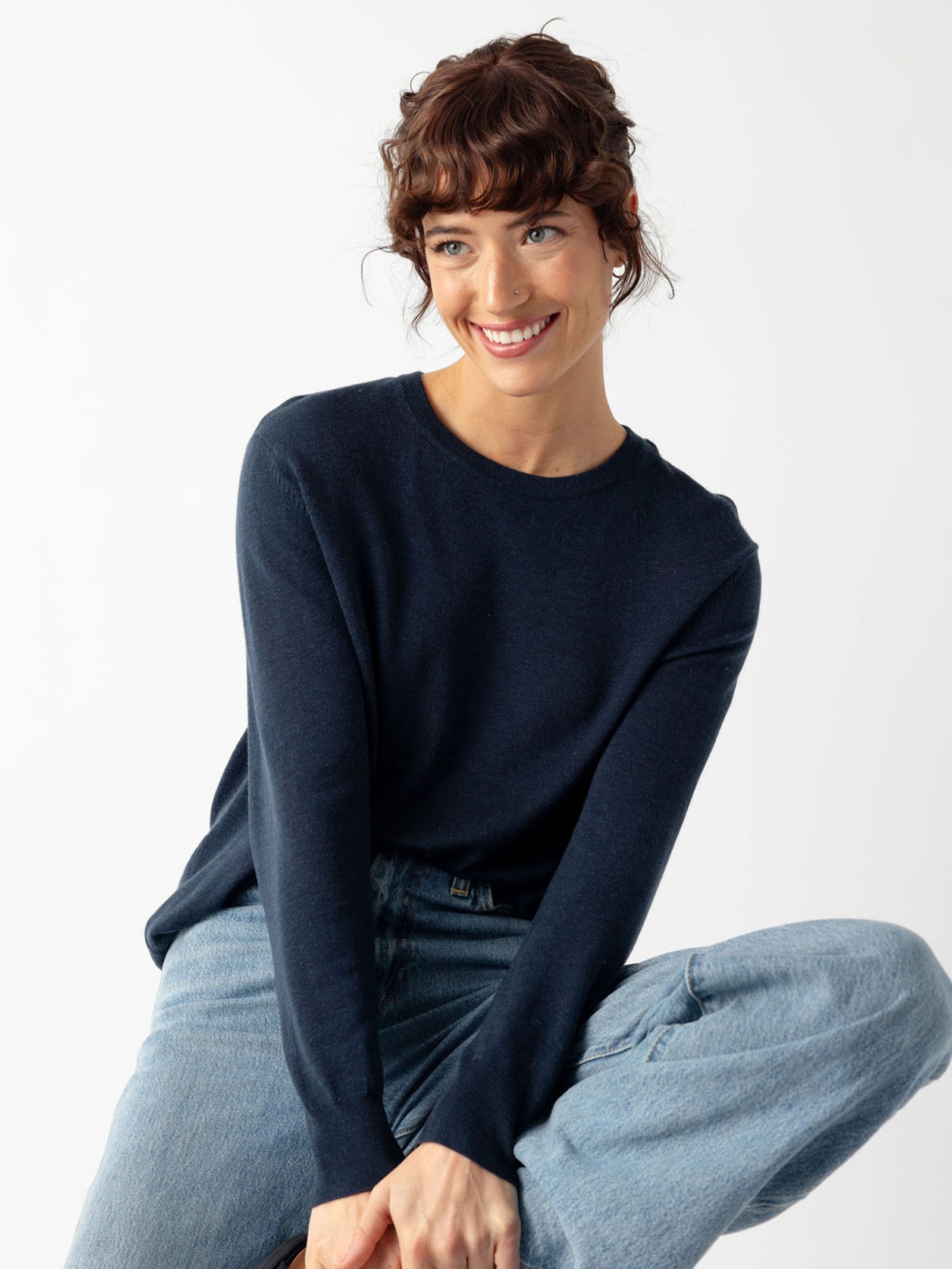 Woman smiling wearing jeans and an eclipse airknit sweater with white background 